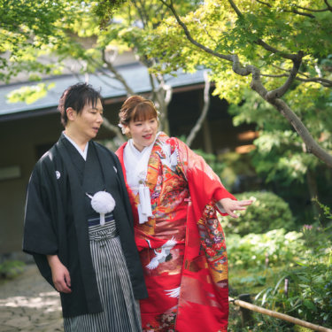 もみじの枝が広がる日本庭園で、寄り添う新郎と庭を指さす色打掛の花嫁。自然な会話を切り取った和装のウェディングフォト