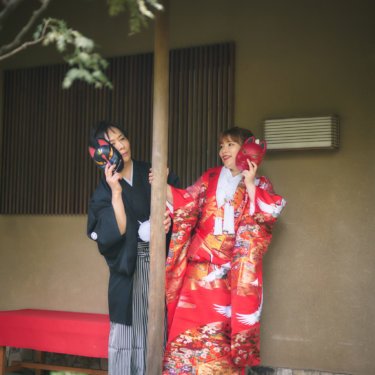 茶室の軒下で狐のお面を顔に当てておどける新郎と色打掛の花嫁。和の小物を使った遊び心ある和装前撮り