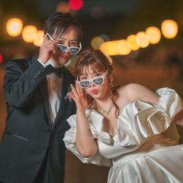 丸の内の街の灯りのボケを背に、サングラスをずらしておどける新郎とパフスリーブのドレスの花嫁。笑顔あふれるナイトフォトウェディング
