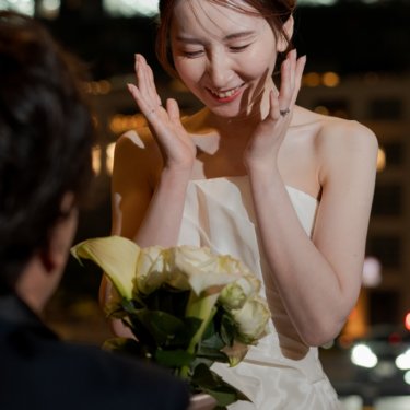 ティアラをつけた花嫁が頬に両手を添えて照れ笑いする、指輪をはめた手元も写る夜の前撮り写真