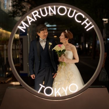 夜の丸の内で'MARUNOUCHI TOKYO'の光るリングオブジェの中に並ぶ新郎と花嫁。おしゃれな夜のフォトウェディング