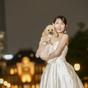 夜の東京駅をぼかした背景で、愛犬のトイプードルを抱いて笑顔を見せるウェディングドレスの花嫁の前撮り