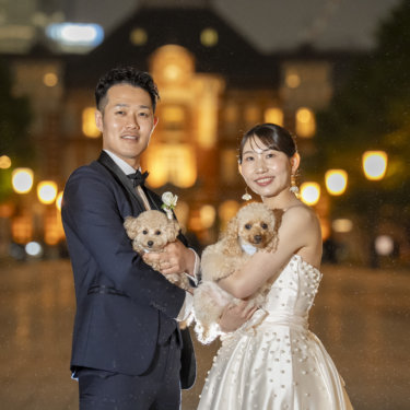 ライトアップされた東京駅を背に、2匹のトイプードルをそれぞれ抱いて笑う新郎新婦。愛犬と撮るフォトウェディング