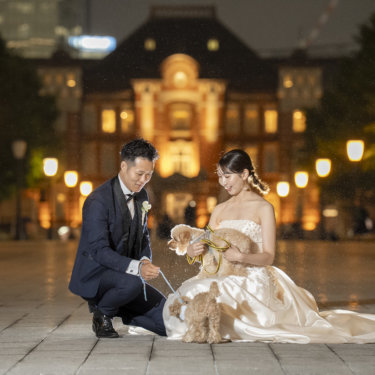 東京駅丸の内駅舎の夜景の前でしゃがみ、リードをつけた愛犬とふれあう新郎新婦のフォトウェディング