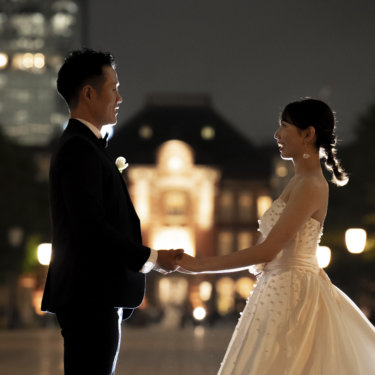 夜の駅舎の明かりを背景に、手を取り合って向かい合う新郎新婦のシルエット気味の夜景ウェディングフォト