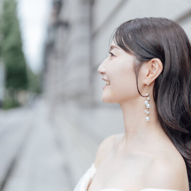 パールのイヤリングを揺らして横を向き微笑む花嫁の横顔。背景をぼかしたシンプルなオフショルダードレスのブライダルポートレートで撮る前撮り