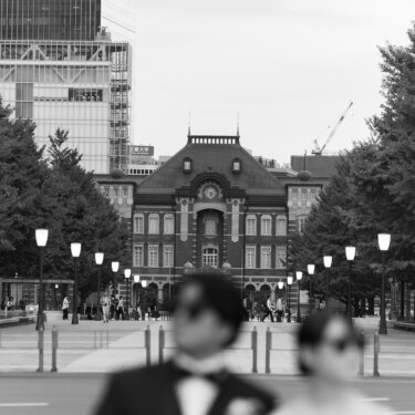 行幸通りの奥に東京駅丸の内駅舎を写し、手前のサングラス姿の新郎新婦をぼかしたモノクロのおしゃれな結婚写真