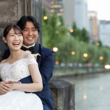後ろからハグされて楽しそうに笑うオフショルダーのドレスの花嫁と新郎。お濠沿いで自然な表情を残す洋装前撮り