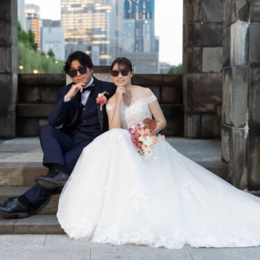 石のアーチの階段に並んで座り、サングラスでポーズを決める新郎新婦。大きく広げたドレスの裾が映えるロケーションフォト