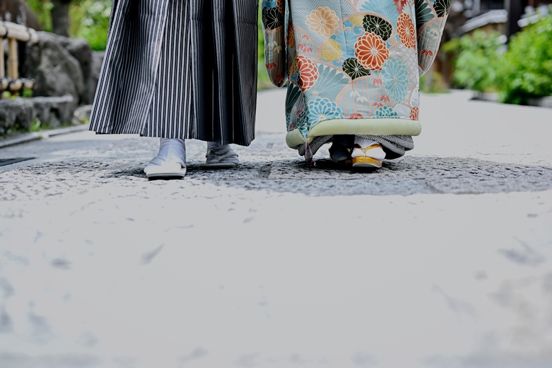 石畳の道に立つ新郎新婦の足元、白と紺の着物姿。