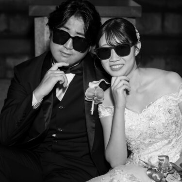 石造りのアーチに腰かけ、サングラスをかけて頬杖をつく新郎新婦をモノクロで写したおしゃれな結婚写真
