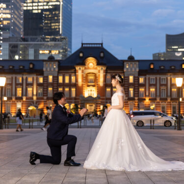 東京駅丸の内駅舎と高層ビルを背景に、片ひざをついて花嫁にプロポーズする新郎。トレーンの長いウェディングドレスが映えるフォトウェディング