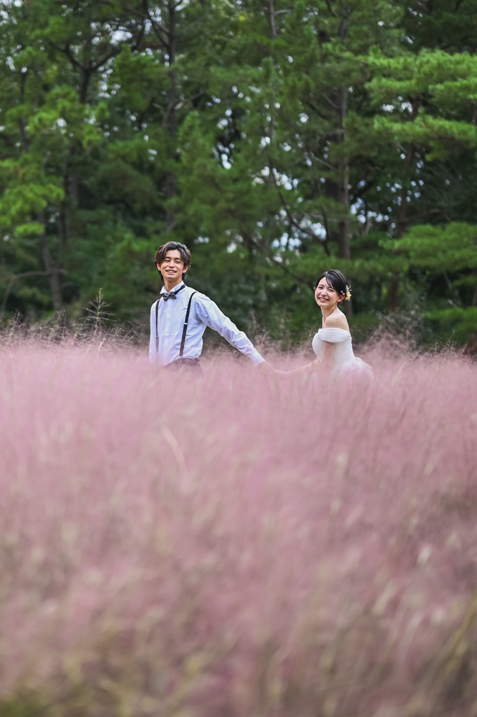 ピンク色のすすき野原で寄り添う洋装の新郎新婦のロケーションフォト。