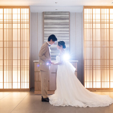 組子格子の和モダンなチャペル全景。長いトレーンを広げたウェディングドレスの新婦と、ベージュのタキシードの新郎が向かい合う結婚写真