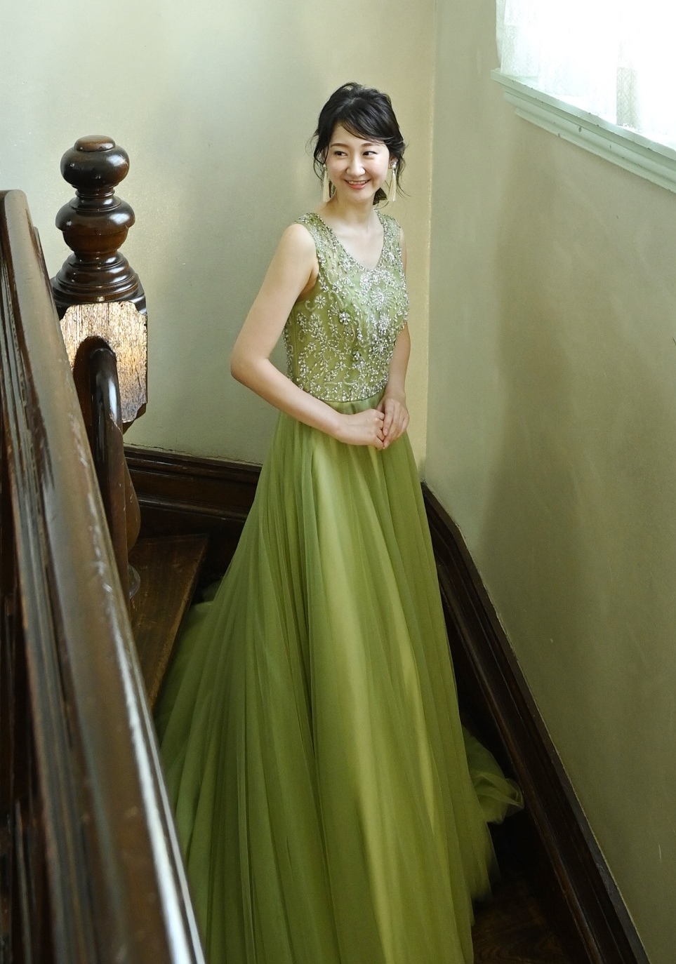 オリーブグリーンのビーズ刺繍ドレスを着た新婦が、階段で微笑むポートレート。