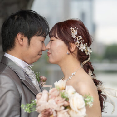 お濠を背に、ピンクのブーケを手におでこを寄せ合うタキシードの新郎と花嫁。水辺で撮るロマンチックなフォトウェディング