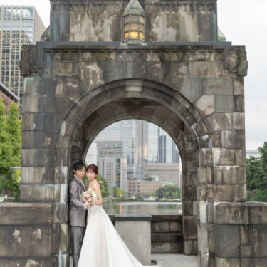 緑の屋根の石造りのアーチ門の下で、長いトレーンを広げて寄り添う新郎新婦。東京駅周辺で撮るクラシカルな洋装前撮り