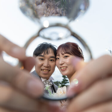 大きなダイヤの指輪のオブジェの中に写り込む、笑顔の新郎新婦。アイテムを使ったユニークなフォトウェディング