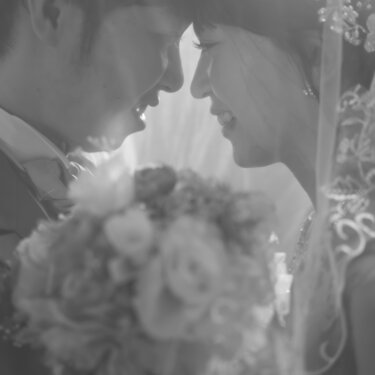 ブーケ越しにおでこを寄せ合いほほえむ新郎新婦をモノクロで写した一枚。クラシカルな洋装フォトウェディング